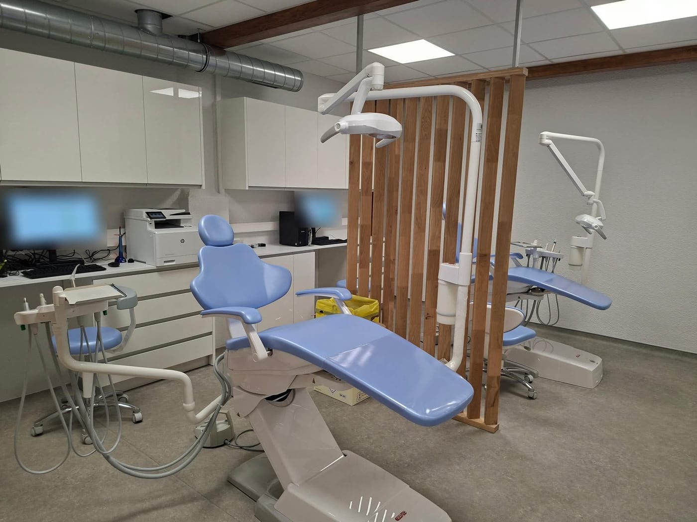 Salle de soins : deux fauteuils dentaires bleus séparés par une cloison en lattes de bois